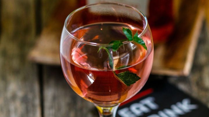 Ein elegantes Glas mit rosafarbenem Getr&auml;nk steht auf einem Holztisch, umgeben von einem BBQ-Schild, voller Genuss und festlicher Stimmung.