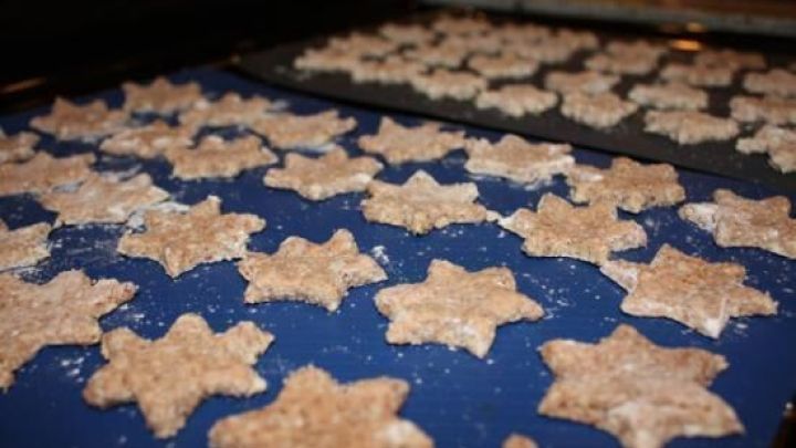 Sternf&ouml;rmige Zimtsterne liegen ungebacken auf einem blauen Backblech, bereit f&uuml;r den Ofen. Im Hintergrund ein weiteres Blech.