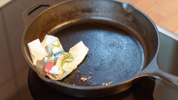 Eine Gusseisen-Pfanne liegt auf einem Herd und wird mit einem Papiertuch gereinigt. Der Raum wirkt sauber und aufger&auml;umt.