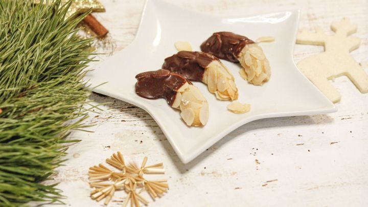 Drei Marzipan-Mandel-H&ouml;rnchen liegen auf einem sternf&ouml;rmigen Teller, umgeben von Tannenzweigen und Dekoration.