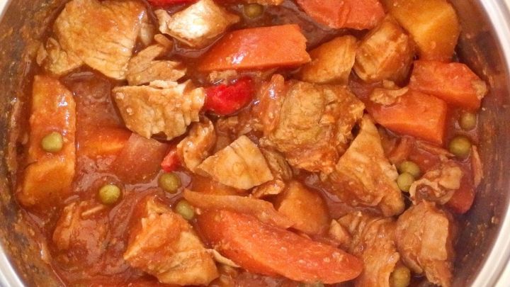 Ein zartes Gulasch mit Zwiebeln und buntem Gem&uuml;se kocht in einem Topf, umgeben von einer warmen K&uuml;che.