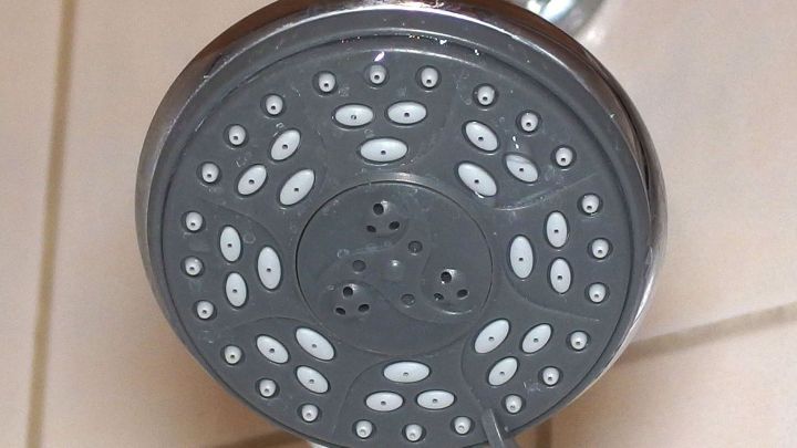 Der verkalkte Brausekopf zeigt, wie Wasser durch die verstopften D&uuml;sen flie&szlig;t, um in einem Badezimmer zu sprudeln.