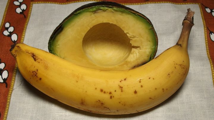 Eine auf einem Tuch liegende Banane neben einer halbierten Avocado, bereit f&uuml;r eine cremige Zubereitung.