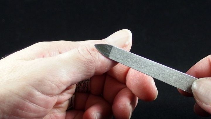 Eine Hand h&auml;lt eine Nagelfeile, w&auml;hrend sie vorsichtig versucht, Sekundenkleber von der Haut zu entfernen.