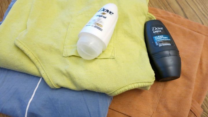 Deo-Roll-ons von Dove liegen auf gestapelten, farbigen Kleidungsst&uuml;cken auf einem Holztisch.