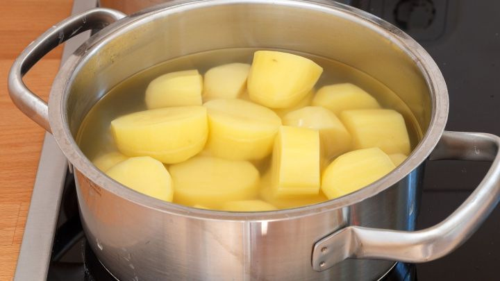 Kartoffeln kochen im Metalltopf auf modernem Herd; gelbe Kartoffelst&uuml;cke in Wasser umgeben von Holz- und Glaskeramik.