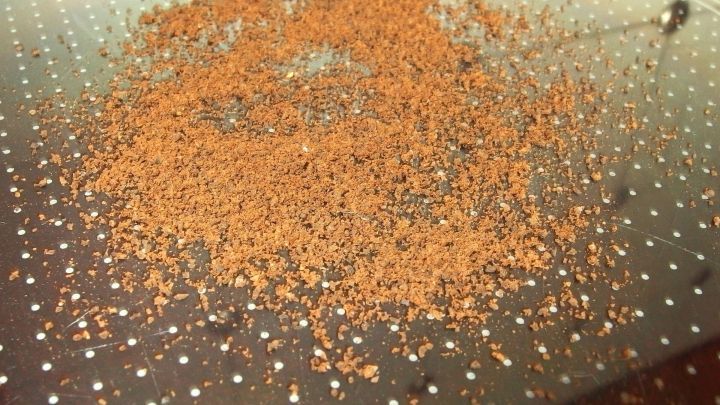 Ein Haufen brauner Gew&uuml;rze liegt auf einer glatten, perforierten Oberfl&auml;che und deutet auf intensives Kochen hin.