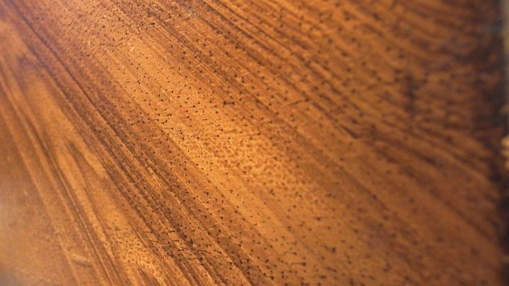 Ein glattes St&uuml;ck Holz zeigt die feinen Maserungen, die Kerzenwachs darauf verteilt hat, in einem hellen Raum.