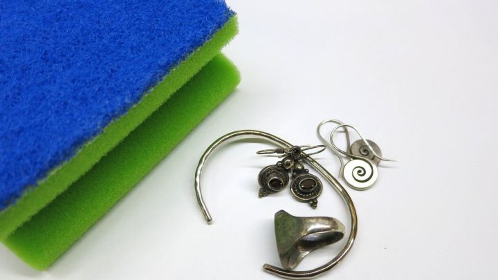 Silbernen Schmuck liegt neben einem Reinigungsschwamm auf einer wei&szlig;en Unterlage, bereit zum Matt halten und reinigen.