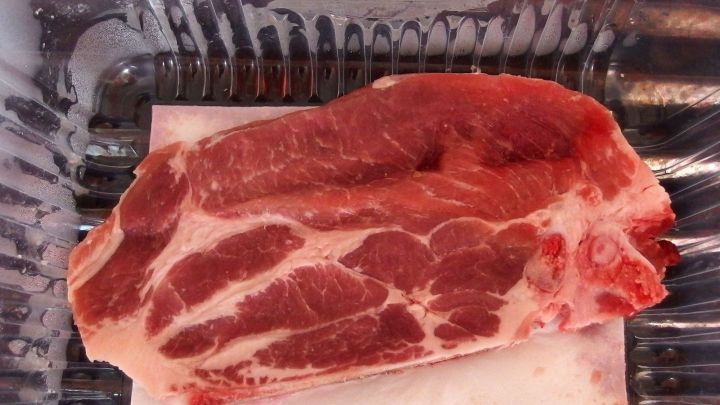 Eine frische Fleischscheibe liegt auf einer Plastikunterlage in einem transparenten Beh&auml;lter und zeigt eine ansprechende Marmorierung.