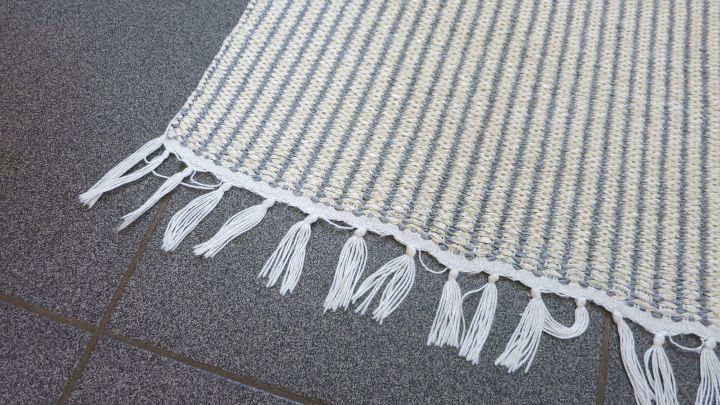 Ein Teppich mit Fransen liegt auf einem grauen Boden, wobei die Fransen auff&auml;llig klar und gepflegt erscheinen.