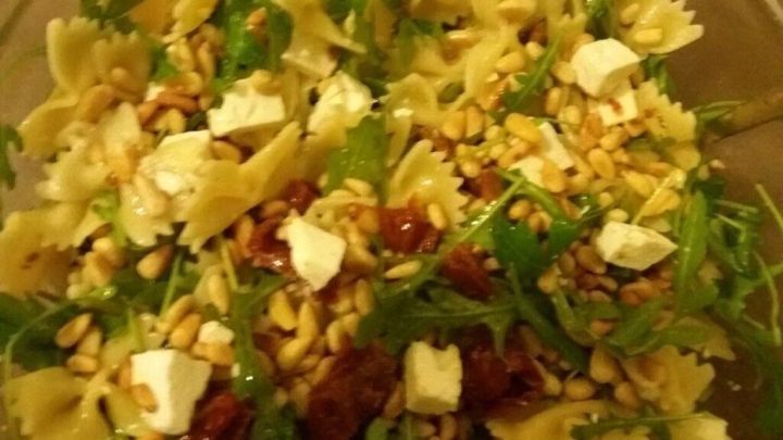 Ein bunter Nudelsalat mit Rucola, eingearbeitet mit Feta, Pinienkernen und getrockneten Tomaten in einer Sch&uuml;ssel.