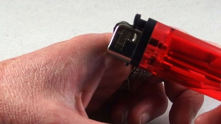 Eine Hand h&auml;lt ein rotes Feuerzeug, das kurz davor ist, angez&uuml;ndet zu werden, um Hitze bei Insektenstichen zu erzeugen.