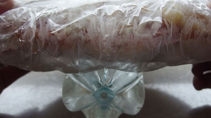 Eine Pizza, in Folie eingewickelt, wird vorsichtig gehalten und auf einem Flaschenverschluss abgestellt, bereit f&uuml;r den Miniofen.