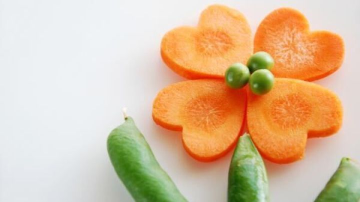 Eine Blume aus M&ouml;hren liegt auf einem hellen Hintergrund, umgeben von Erbsen, die eine kreative Snackpr&auml;sentation zeigen.