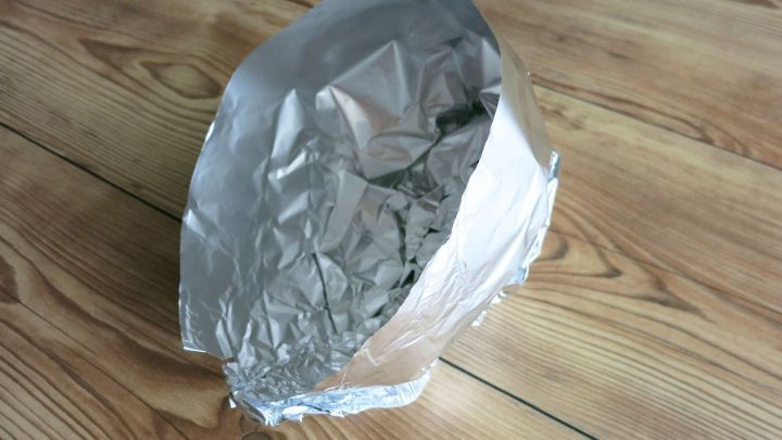 Ein schicker Hut aus Alufolie steht auf einem holzernen Boden und wirkt seltsam und humorvoll.