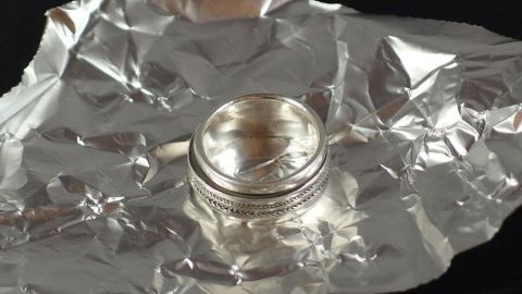 Damit silberner Schmuck nicht anläuft, kann man ihn in Alufolie verpackt aufbewahren. Ein glänzender Ring liegt auf zerknitterter Alufolie, die ihn umgibt und schützt. Ein einfacher, effektiver Schmuckschutz.