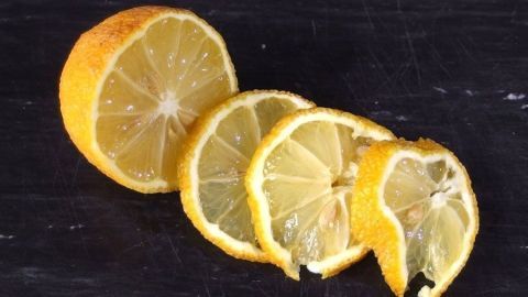 Schrumpelige und hart gewordene Zitronen nicht wegschmeißen, sondern in Scheiben schneiden und einfrieren. Kann dann in jedes beliebige Getränk gegeben werden. Zitronenscheiben liegen auf einer dunklen Oberfläche, bereit, als kühle Eiswürfel verwendet zu werden.