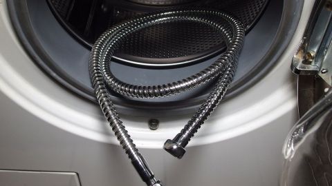 Flexible Duschschläuche liegen neben einer Waschmaschine, bereit zur Reinigung von Kalkablagerungen.