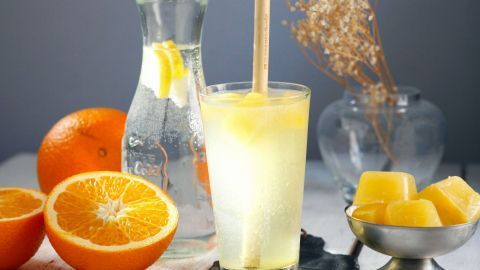 Das perfekte Sommergetränk ist ganz einfach mit gefrorenem Fruchtsaft zubereitet. Es ist lecker, kühl und erfrischend. Ein frischer Drink aus echter Fruchtler und Eiswürfeln wird in einem Glas serviert, umgeben von Orangen und elegantem Zubehör.