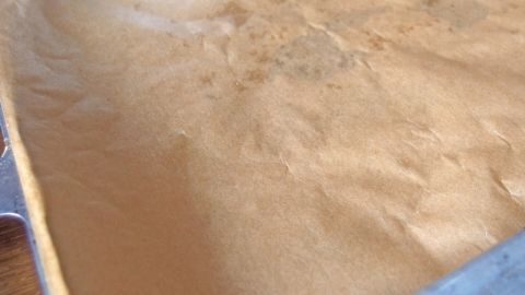 Eine bessere Haftung für Backpapier auf dem Backblech bekommt man, wenn man etwas Öl auf das Blech gibt. Ein Blatt Back-Papier liegt auf einem Blech und zeigt eine glatte, leicht gefärbte Oberfläche, bereit zum Backen.