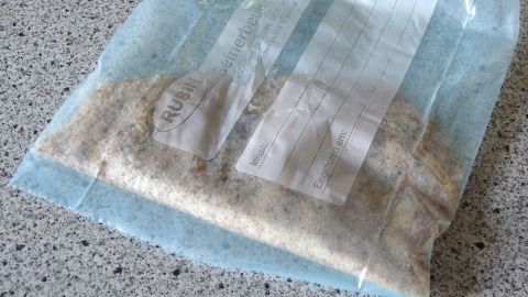 Ein Gefrierbeutel enthält panierte Schnitzel. Darin wird gerade die Panade gleichmäßig verteilt. Der Untergrund ist eine Küchenarbeitsplatte.