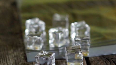 Kristallklare Eiswürfel liegen auf einer Holzoberfläche und scheinen für die Zubereitung eines kühlen Drinks bereit zu sein.