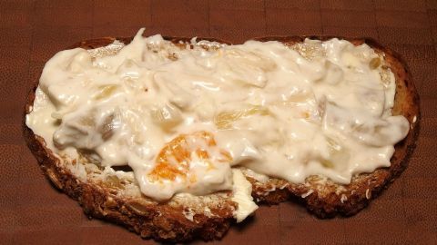 Ein belegtes Brot ist mit einer cremigen Geflügelsalat-Mischung bedeckt, in einer rustikalen Umgebung aus Holz.