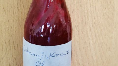 Eine kleine Flasche mit Johanniskrautöl steht auf einem Holzuntergrund, bereit zur Behandlung von Hautreizungen.