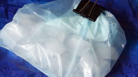 Bereite Eiswürfel auf Vorrat zu, indem du einen Gefrierbeutel mit einem Clip sicher verschließt. Ein praktischer Tipp, um jederzeit gut gekühlte Getränke genießen zu können, ohne ständig neue Eiswürfel machen zu müssen. Eine Plastiktüte gefüllt mit Eiswürfeln ist mit einer Klammer verschlossen und liegt auf einer blauen Unterlage.