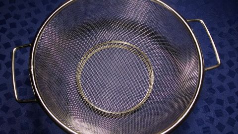 Ein Mehlsieb liegt auf einem blauen Stoff, bereit zum Reinigen, um feines Mehl gleichmäßig zu sieben und Klumpen zu vermeiden.