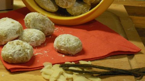 Kleine Vanillekipferl-Kugeln liegen auf einem roten Tuch, während weitere in einer gelben Schüssel im Hintergrund wohnen.