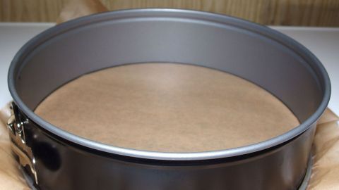 Eine Springform mit Backpapier im Inneren liegt auf einer Arbeitsfläche, bereit zum Backen von Kuchen oder Torten.