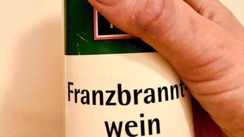 Eine Hand hält eine Flasche mit Franzbranntwein, bereit zur Anwendung gegen Schuppen in einem hellen Hintergrund.