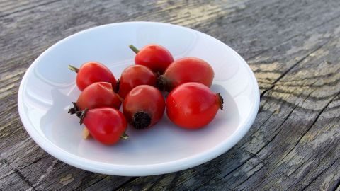 Rote Hagebutten liegen auf einem weißen Teller, umgeben von einer rustikalen Holzoberfläche und strahlen Vitalität aus.