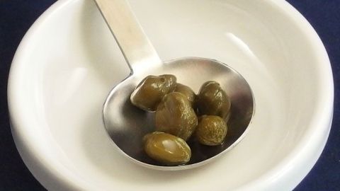 Kapern liegen in einer kleinen Schüssel, während ein Löffel bereit ist, sie zum Zerkleinern aufzugreifen.