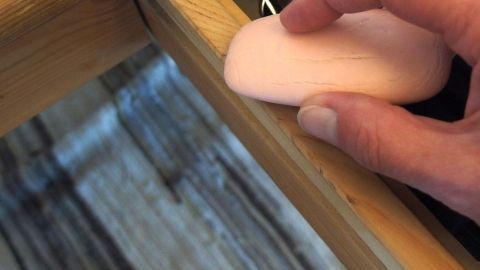 Eine Hand hält einen Schwamm, der über eine Holzschublade bewegt wird, um sie leichter gängig zu machen.