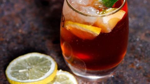 Ein Glas Calimocho aus Rotwein und Cola steht auf einer rustikalen Oberfläche, begleitet von frisch geschnittenen Zitronenscheiben.