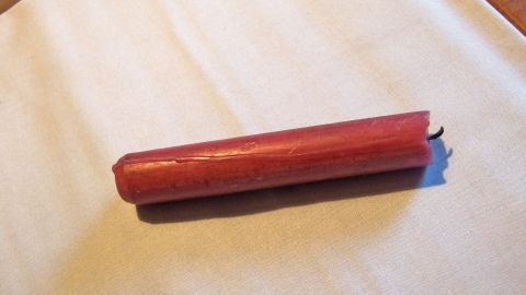 Fragst du dich, wie du Wachsflecken aus der Tischdecke entfernen kannst? Dann hilft dir dieser Tipp dabei. Eine rosa Kerze liegt auf einer Tischdecke und hinterlässt potenziell Wachsflecke. Die Umgebung wirkt gemütlich und heimisch.