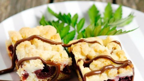 Zwei Stück Hefekirschkuchen mit Streusel liegen auf einem weißen Teller, garniert mit Schokolade und frischen Blättern.