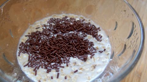 Eine Schüssel mit Haferflocken-Joghurt, bedeckt mit Schokoladenstreuseln, steht auf einem Holzuntergrund.