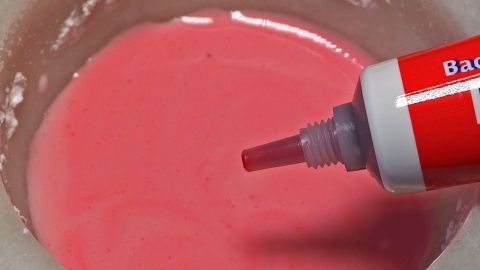 Ein roter Dekorationsstift drückt farbigen Puderzucker in eine schüsselförmige Mischung aus pinkem Zuckerguss.
