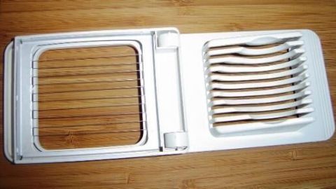 Ein Gemüseschneider mit dünnen Metallfäden, geöffnet auf einem Holztisch, kann zum Bratkartoffeln schneiden dienen.