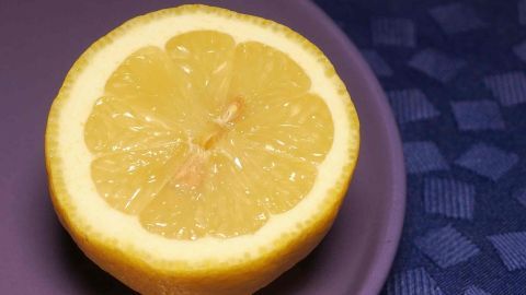 Eine halbierte Zitrone liegt auf einem lila Teller, bereit, frischen Zitronensaft für eine Zuckerfreie Zitronenlimo zu liefern.