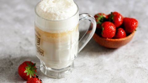 Ein Glas mit Erdbeerjoghurt steht auf einem hellen Untergrund, umgeben von frischen Erdbeeren in einer Schüssel.