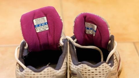 Bei Joggingschuhen kann man das Herstellungsjahr in der Lasche herausfinden. So kauft man nie aus Versehen das alte Modell! Zwei Joggingschuhe stehen auf einem Boden, die Fersen sind sichtbar, mit einem lila Polstering.