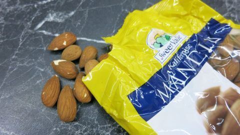 Süße oder geriebene Mandeln wirken vorbeugend gegen Sodbrennen! Süße Mandeln liegen um eine geöffnete Packung auf einer dunklen, marmorierten Oberfläche und könnten gegen Sodbrennen helfen.