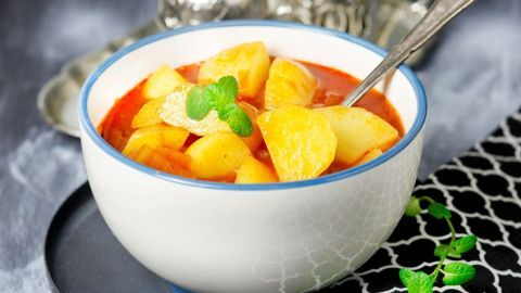 Eine Schüssel mit türkischer Kartoffelsuppe zeigt Stücke von Kartoffeln in einer roten Brühe, dekoriert mit Minze.