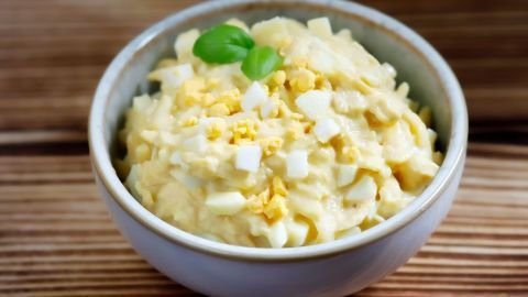 Ein cremiger Senf-Apfel-Dip in einer Schüssel, garniert mit frischen Kräutern, auf einem rustikalen Holzuntergrund.