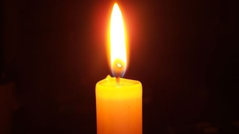 Eine einzelne brennende Kerze leuchtet ruhig in dunkler Umgebung, ihr gelbes Wachs schimmert im warmen Licht der Flamme.